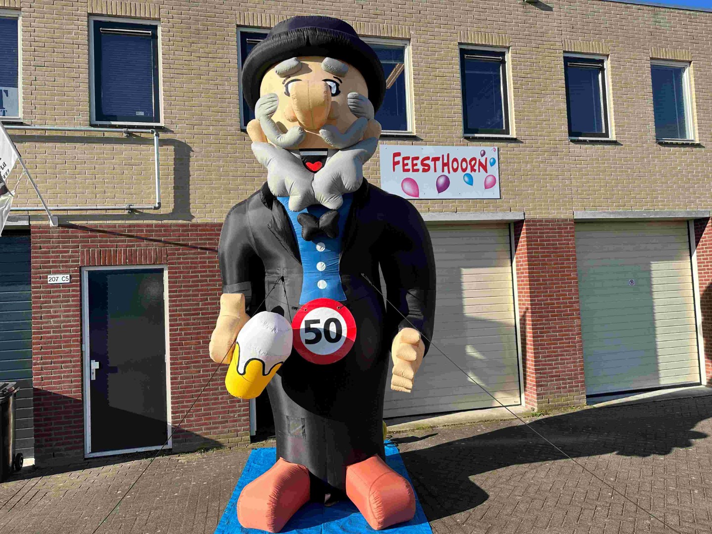 De Abraham Cartoon XL met een bierpul in de hand. Heeft een hoogte van 4.2 meter. Wordt standaard geleverd met een ’50’ verkeersbordbanner. Er is eventueel ook keuze uit een ander getal of een ‘pensioen’ banner.